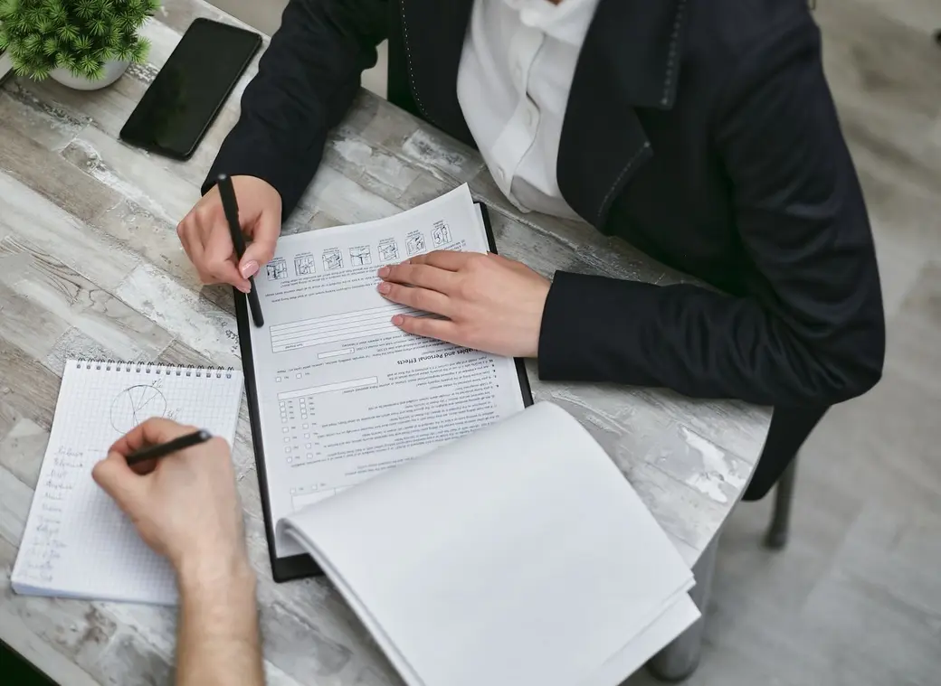 Beraterin und Kunde gehen gemeinsam eine Checkliste mit Unterlagen fuer den Immobilienverkauf durch